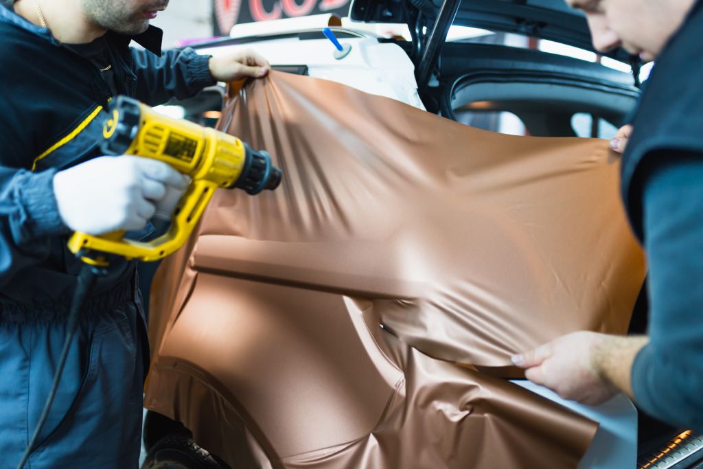 Car wrapping specialist putting vinyl foil or film on car. Selective focus.
