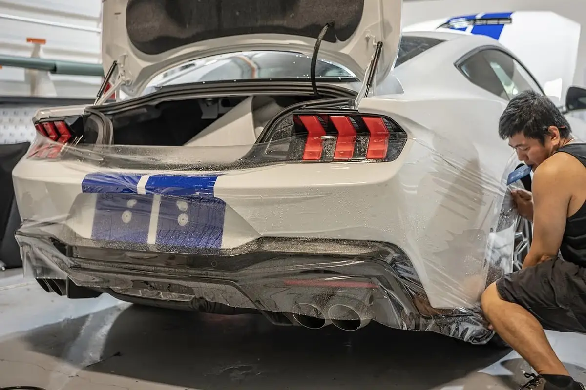 Worker installing paint protection film (PPF) on Ford Mustang in Sydney worksho